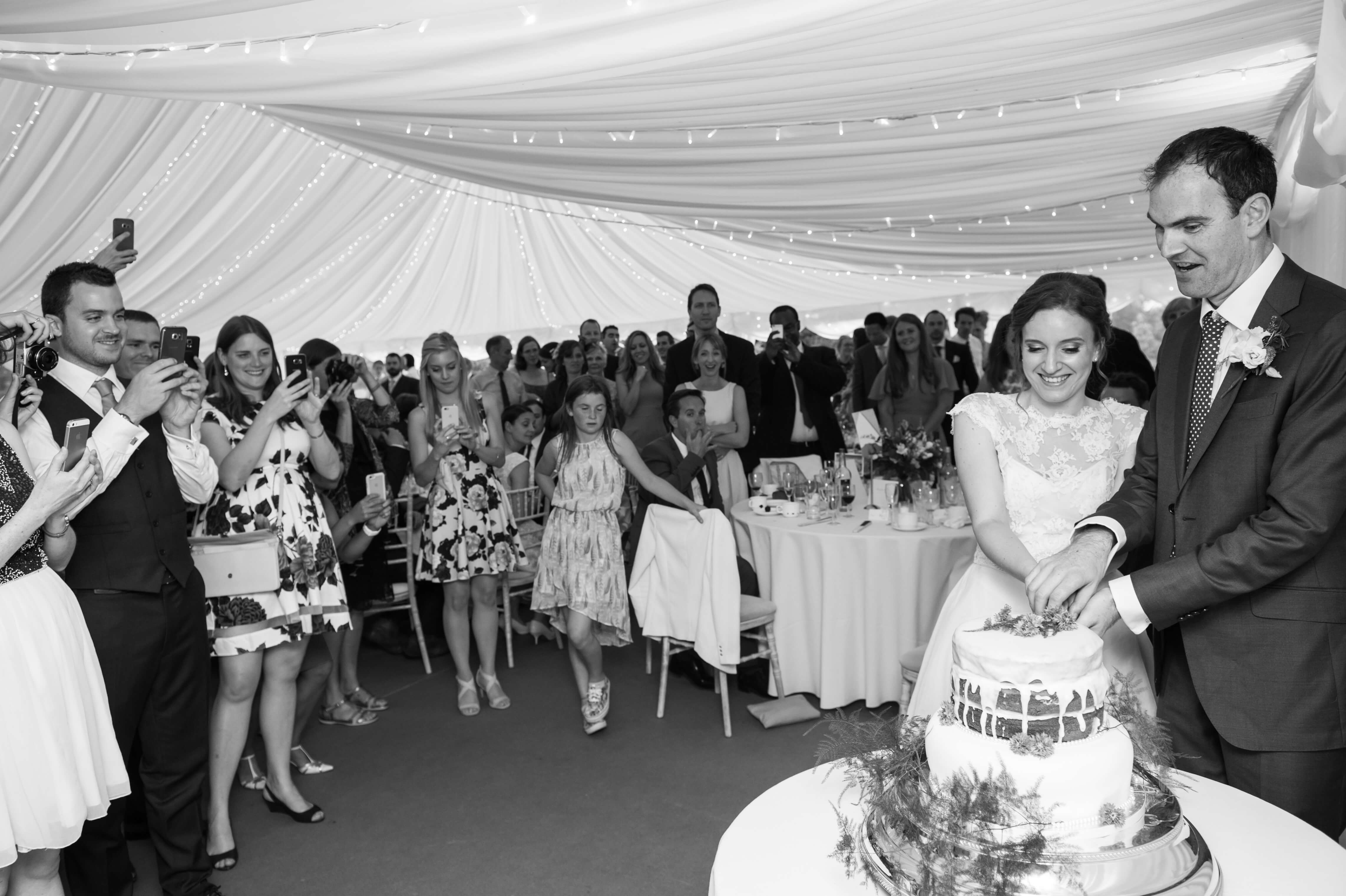 A bride and groom cutting the cake in a marquee at Kingston Bagpuize House